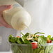 A person using a Vollrath clear squeeze bottle to pour dressing onto a salad.