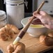 A person using a Carlisle Sparta Spectrum pastry brush to glaze croissants.