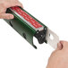A hand holding a green and red metal strip to cut a piece of paper.