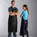 A man and woman wearing Choice black vinyl dishwasher aprons in a professional kitchen.