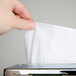 A hand using a Vollrath stainless steel in-counter minifold napkin dispenser to grab a tissue.