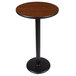 A Lancaster Table & Seating bar height table with a round walnut and oak top on a black cast iron base.
