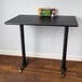 A black Lancaster Table & Seating bar height table with a reversible cherry/black table top and black cast iron base plates.