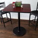 A Lancaster Table & Seating bar height table with a reversible cherry and black table top and a round cast iron base plate.