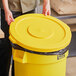 A person holding a yellow Lavex round commercial trash can lid.