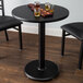 A Lancaster Table with a 24" Round Reversible Cherry / Black Table Top and a drink on a coaster.