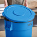 A person holding a blue Lavex 44 gallon commercial trash can lid.