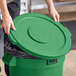 A person opening a Lavex green commercial trash can lid.
