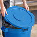 A person holding a Lavex blue round commercial trash can lid.