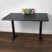 A black Lancaster Table & Seating table with a cherry/black reversible top and a black cast iron base.