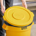 A person placing a yellow Lavex trash can lid on a yellow garbage can.
