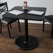 A Lancaster Table & Seating black table with a reversible cherry/black top on a round cast iron base with two chairs and a menu on it.