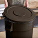 A man placing a brown Lavex round commercial trash can lid on a trash can.