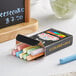 A box of 12 Choice assorted colored chalk next to a chalkboard.