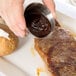 A person using an American Metalcraft stainless steel sauce cup to pour sauce over a steak.