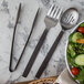 A bowl of salad with American Metalcraft wavy stainless steel salad utensils on a marble surface.