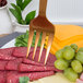 An American Metalcraft hammered bronze cold meat fork with a piece of meat and cheese on it.
