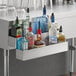 A Regency double tier stainless steel speed rail on a counter filled with liquor bottles.
