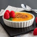 A Tuxton eggshell oval fluted dish of creme brulee with raspberries.