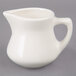 A Tuxton eggshell white china creamer with a handle on a gray surface.