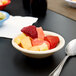 A Carlisle tan melamine fruit bowl filled with strawberries on a table with a spoon.