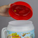 A hand holding a red and white "Fun at the Fair" plastic tanker lid over a white container with a blue and yellow design.