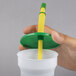 A hand holding a yellow straw in a white cup with a green lid and straw.