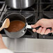 A person stirring a Thunder Group sauce pan with a wooden spoon.