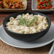 A Tuxton TuxTrendz matte black china bowl filled with pasta and a sprig of rosemary.