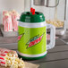 A green and white Mountain Dew Tanker with red straws next to a bag of popcorn.