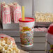 A white plastic cup with a red lid and a cartoon design on it next to a bag of popcorn.