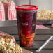 A 32 oz. Coca-Cola plastic cup with a red lid filled with a drink and ice next to a bag of popcorn.