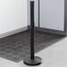A Lancaster Table & Seating black ADA compliant stanchion with dual retractable belts on a black mat.
