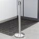 A silver Lancaster Table & Seating crowd control stanchion on a black mat.