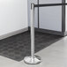A silver Lancaster Table & Seating crowd control stanchion on a black mat.