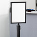 A white sign in a black Lancaster Table & Seating stanchion sign frame.