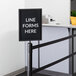 A Lancaster Table & Seating black vertical sign frame attached to a stanchion pole.