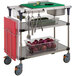 A Metro PrepMate MultiStation kitchen cart with stainless steel shelving holding vegetables and utensils.