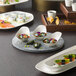 A table with Schonwald bone white porcelain gourmet appetizer spoons filled with food.