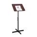 A mahogany and black Safco adjustable speaker stand with a clipboard on it.
