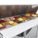 A Turbo Air Super Deluxe refrigerated sandwich prep table with food trays of different types of food on a counter.