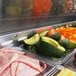 A Turbo Air refrigerated sandwich prep table with trays of meats and vegetables on a counter.