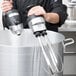 A man using a Waring whisk attachment on a Waring immersion blender in a large pot.