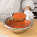 A person using a Vollrath Spoodle to pour red sauce over a bowl of red sauce.