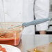 A person using a Vollrath Jacob's Pride Spoodle to serve red sauce from a glass container.
