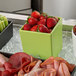 A tray of G.E.T. Enterprises Bugambilia lime salad bowls on a hotel buffet counter filled with strawberries, meat, and vegetables.
