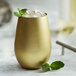 A Stolzle gold stemless wine tumbler filled with ice and mint leaves.
