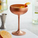 A Stolzle copper coupe glass filled with a cocktail and garnished with an orange peel.