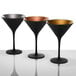 A group of Stolzle matte black martini glasses with gold rims on a white surface.
