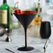 A matte black Stolzle martini glass with a black liquid and red cherries in it.
